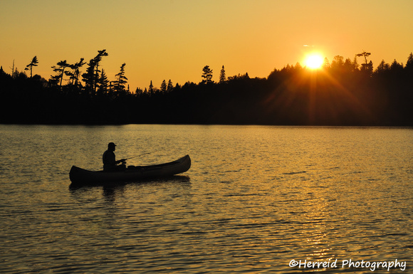 A Man Fishing From a Canoe at Sunset on a Remote Wilderness Lake